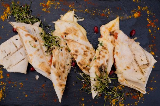 Lavash with cheese on a flat black plate decorated with micro green and pomegranate seeds. Restaurant dish.