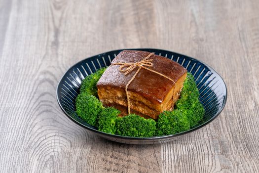 Dong Po Rou (Dongpo pork meat) in a beautiful blue plate with green broccoli vegetable, traditional festive food for Chinese new year cuisine meal, close up.