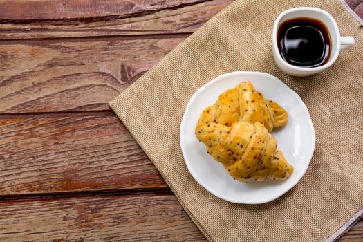 Breakfast concept. Top view croissants with perilla seeds on white plate and white cup of black coffee on wooden table.