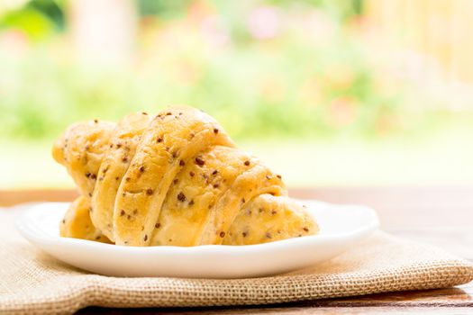 Breakfast concept. Croissants with perilla seeds on white plate and white cup of black coffee on wooden table with green bokeh background.