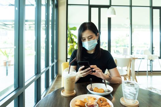 An Asian beautiful woman has to wear a blue mask and prepare to start breakfast in the coffee cafe with new normal and social-distancing.