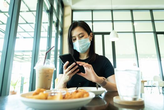 An Asian beautiful woman has to wear a blue mask and prepare to start breakfast in the coffee cafe with new normal and social-distancing.
