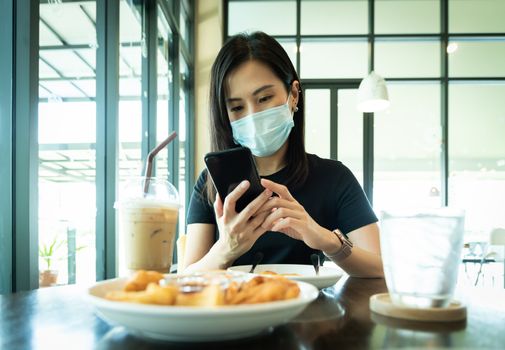 An Asian beautiful woman has to wear a blue mask and prepare to start breakfast in the coffee cafe with new normal and social-distancing.