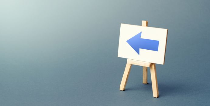 Easel with a blue left arrow. Sign of direction. Advertising of the location of a store or outlet. Minimalism. Restriction of movement, change of course. Short road. Distracting maneuver.