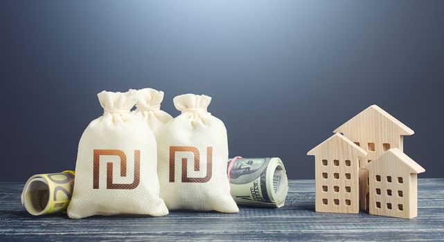 Israeli shekel money bags and residential buildings figures. Financing the construction of new settlements. Municipal budget management. Investments in real estate. Mortgage loan. Taxes.
