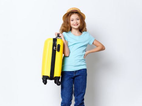 Happy girl with a yellow suitcase holds his hand on his belt and smiles at the camera