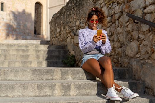 Portrait of an attractive young black woman taking a selfie with her mobile. Talking on the phone sitting on the stairs