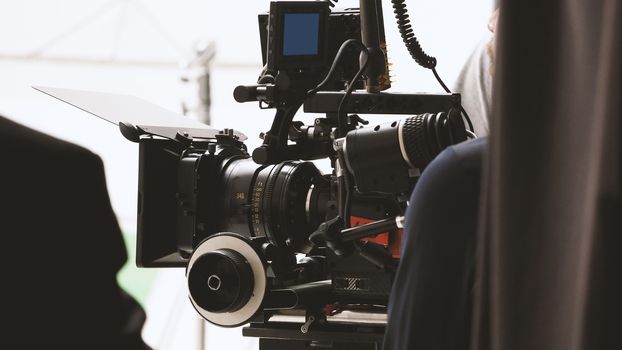 Behind the shooting or filming video movie and film production crew team setting up camera on tripod and professional equipment in studio for offline tv commercial or online web film recording.