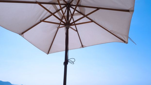 White fabric color texture beach umbrella and brown wood tripod with white cloud and clear blue sky summer sunlight day in low angle view camera for travel asia Thailand Pattaya.