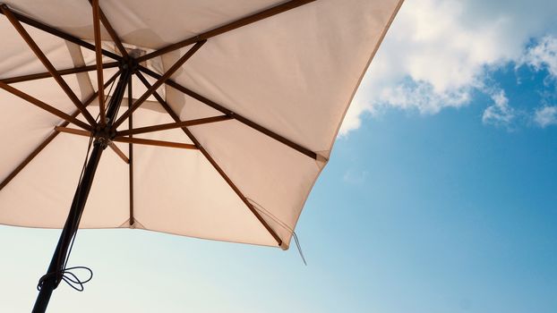 White fabric color texture beach umbrella and brown wood tripod with white cloud and clear blue sky summer sunlight day in low angle view camera for travel asia Thailand Pattaya.