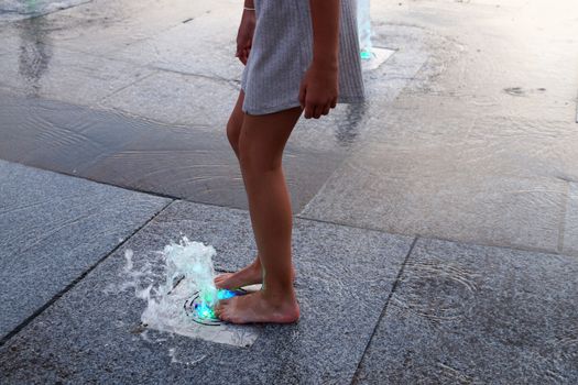 barefoot girl touching the fountain on the sidewalk in the evening.