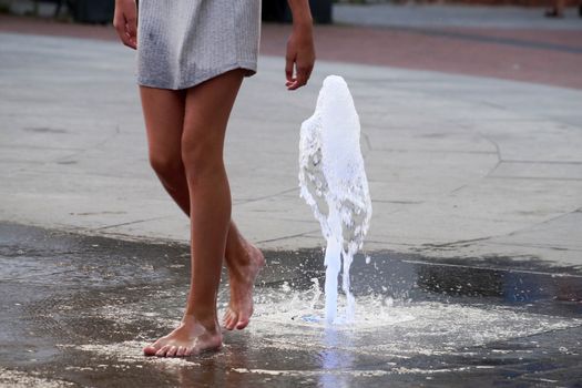 barefoot girl touching the fountain on the sidewalk in the evening.