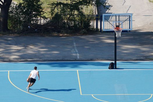 Varna, Bulgaria - August, 22, 2020: young man training with a ball on an outdoor basketball court