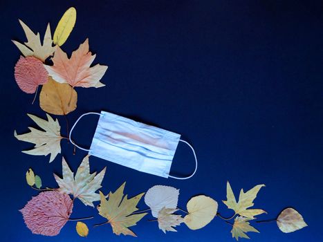 medical mask and autumn leaves on blue background text back to school