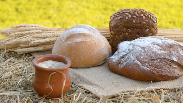 Close up loafs of traditional baked bread, ripe wheat ears and clay pot on jute burlap. Natural organic handmade food