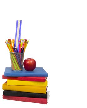 Vertical shot of a stack of colorful books with an apple and a wire pencil holder sitting on top.  Pencil holder is holding pencils and a ruler.  Isolated on white.  Copy space on the right side and the top.