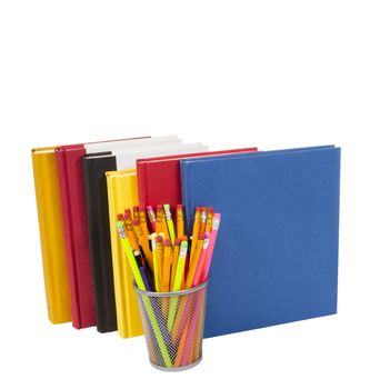 Vertical shot of a group of colorful books standing up with a wire pencil holder in front full of pencils.  White background.  Copy space.