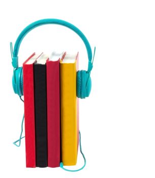 Vertical shot of four colorful books standing on end with a pair of turquoise headphones plugged into them.  Isolated on white.  Copy space. 
