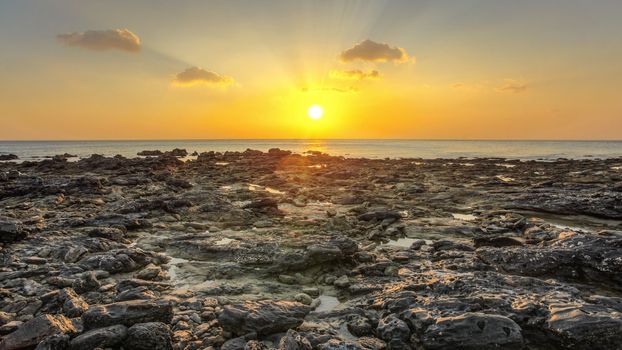 Rocky beach uncovered in low tide during evening sunset light with some clouds over horizon. Koh Lanta, Thailand