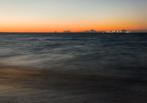 Long exposure shot of dark sea with ships pier illuminated by lights in the evening, and orange sunset sky. Progreso, Mexico