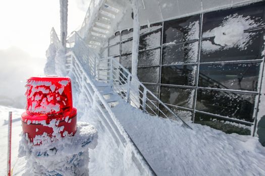 Red emergency lighting with snow and ice covered stairs and windows at top of mountain Chopok ski resort, illustrating extreme cold in the winter. Jasna, Slovakia.