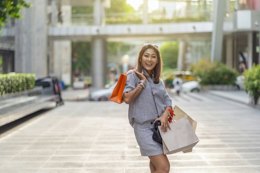 Portrait of Happy Asian woman walking and holding the shopping bag in downtown around shopping center, fashion concept