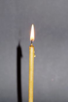 lighted wax candle with shadow on gray background close up