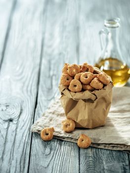 Traditional italian snack taralli or tarallini in paper bag over old gray wooden table. Rustic shot of taralli appetizer with copy space. Vertical