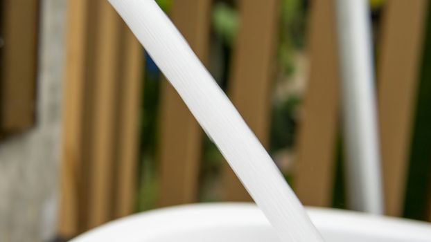 Jet stream of water running from faucet to wash basin with wooden fence background in the outdoor area of a swimming pool.