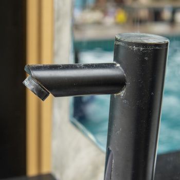 Dust covered modern black color faucet of a wash basin in the outdoor wash area of a swimming pool