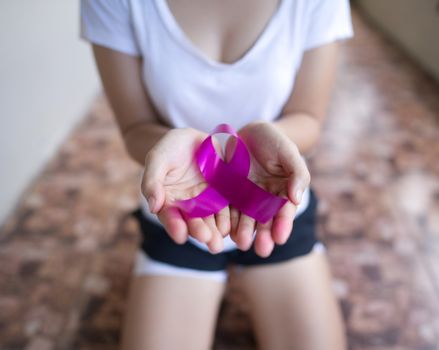 A girl kneeling in her hand holding a pink ribbon showing signs of encouragement concept for breast cancer awareness day.