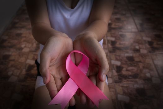 A girl kneeling in her hand holding a pink ribbon showing signs of encouragement concept for breast cancer awareness day.