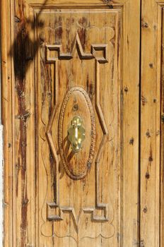 Close-up view of a wooden door with old-fashioned door knocker made of brass.