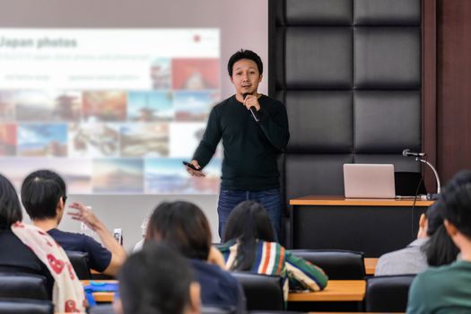 Asian Speaker or lecture with casual suit on the stage presenting via projector screen in the conference hall or seminar meeting room to Audience, business education and Seminar concept