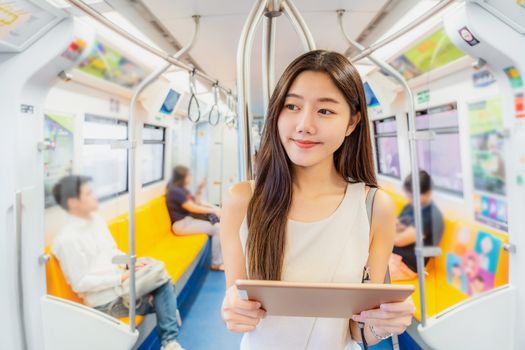 Young Asian woman passenger using mutimedia player via Technology tablet in subway train when traveling in big city,japanese,chinese,Korean lifestyle and daily life,commuter and transportation concept