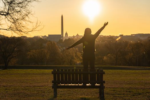 Back side of asian woman standing and Lifting hands for success over the Washington DC Landmark which can see United states Capitol, washington monument and lincoln memorial at the sunrise time,