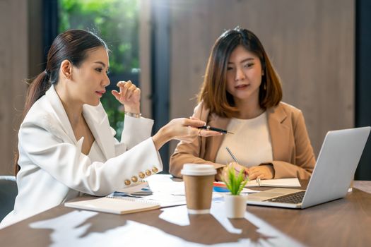 Two asian businesswomen working with the partner business by point pen to the technology laptop in modern meeting room, office or working space, coffee break, partner and colleague concept