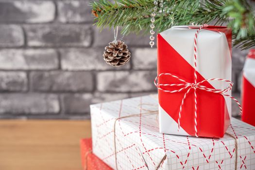 Decorated Christmas tree with wrapped beautiful red and white gifts at home with black brick wall, festive design concept, close up.