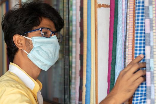 Young man with medical mask selecting or buying cloth at store during coronavirus or covid-19 pandemic - Concept of new normal, business reopen and support local community after lock down