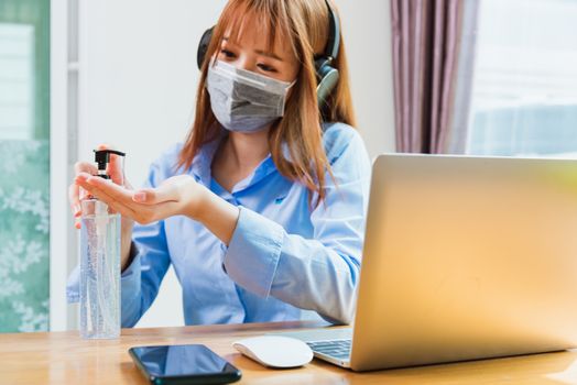 Asian young business woman wearing face mask protective working from home office with laptop computer he quarantines disease coronavirus or COVID-19 and cleaning hands with sanitizer alcohol gel pump