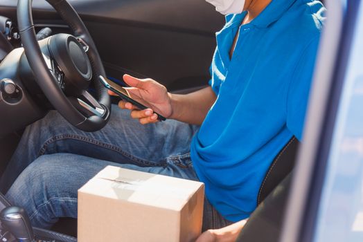 Asian delivery man courier online holding deliveries out boxes in car and using mobile phone contact the customer he protective face mask service under curfew quarantine pandemic coronavirus COVID-19