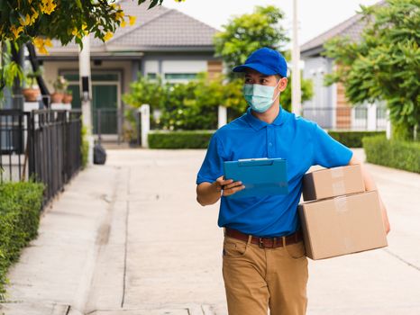 Asian young delivery man courier hold parcel post boxes he protective face mask service and walk looking for customer home location, under curfew pandemic coronavirus COVID-19