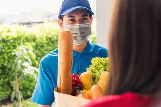 Asian young delivery man in uniform wear protective face mask he making grocery service giving fresh food to woman customer receiving front house under pandemic coronavirus, Back to new normal concept