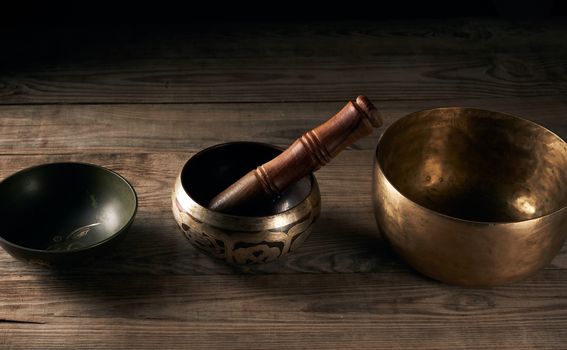 Tibetan singing copper bowl with a wooden clapper on a brown wooden table, objects for meditation and alternative medicine