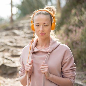 Portrait of beautiful sports woman with hoodie and headphones during outdoors training session. Healthy lifestyle image of young caucasian woman jogging outside.