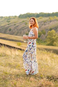 Beautiful red-haired girl is having fun and dancing in a field at sunset.