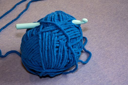 A plastic crochet hook is pushed through a large ball of thick blue yarn meant for making blankets.