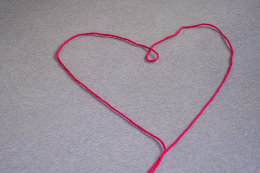 A single thread of pink yarn forms the shape of a heart, laid out on a flat fabric surface.