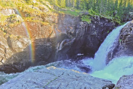 Fallen dead and broken tree beside rainbow over the canyon from Rjukandefossen waterfall.