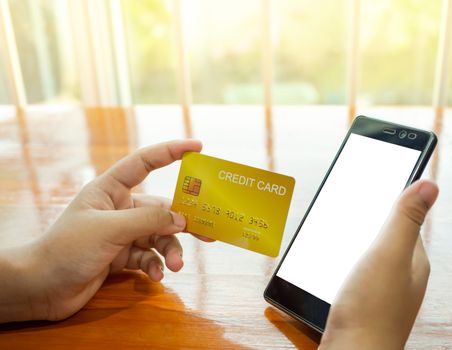 OOnline shopping concept with human hand holding smart phone and credit card on wood table and window background.